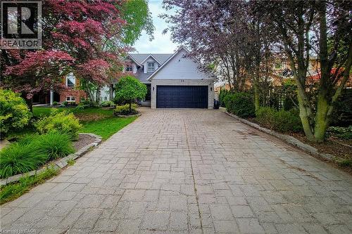 Paved driveway featuring a two-car garage, brick and siding exterior, multiple dormer windows, and mature landscaping - 29 Woodside Square, Fonthill, ON - Outdoor