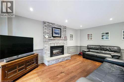 Living area featuring a brick-clad fireplace with a stone hearth, recessed lighting, wood-finish flooring, and wainscoting - 29 Woodside Square, Fonthill, ON - Indoor Photo Showing Living Room With Fireplace