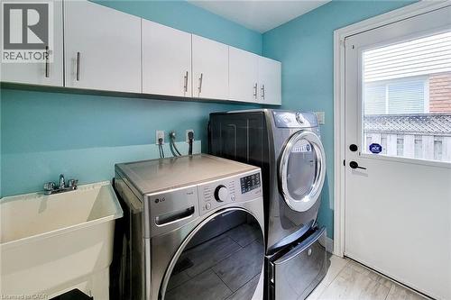 Laundry area featuring white upper cabinetry with brushed nickel hardware, a utility sink with dual-handle faucet, and light-toned flooring - 29 Woodside Square, Fonthill, ON - Indoor Photo Showing Laundry Room