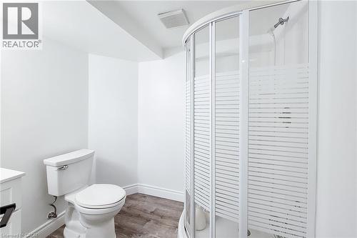 Bathroom featuring a curved shower enclosure with frosted louvered panels, a white toilet, wood-finish flooring, and white baseboards - 29 Woodside Square, Fonthill, ON - Indoor Photo Showing Bathroom