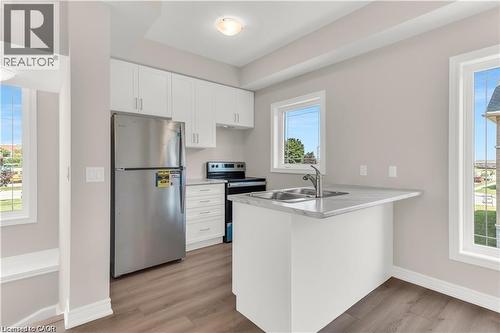 Kitchen featuring wood-finish flooring, white cabinetry, a stainless steel refrigerator, and a kitchen island with a double basin sink and a light-toned countertop - 19 Picardy Drive Unit# 9, Hamilton, ON 