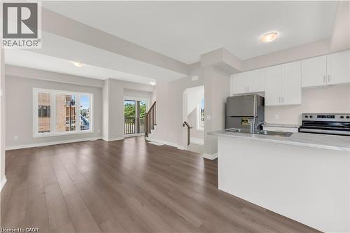 Open-concept living space featuring wood-finish flooring, a kitchen peninsula, white cabinetry, stainless steel appliances, and a sliding glass door leading to a balcony - 19 Picardy Drive Unit# 9, Hamilton, ON 