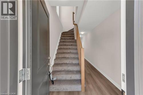 Entryway featuring a contemporary gray front door, light wood-finish flooring, and a carpeted staircase with a natural wood railing - 19 Picardy Drive Unit# 9, Hamilton, ON 