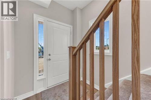 Entryway featuring a white paneled door with sidelight, wood-finish flooring, and a natural wood-finish staircase railing with carpeted steps - 19 Picardy Drive Unit# 9, Hamilton, ON 