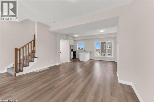 Spacious open-concept living area featuring wood-finish flooring throughout, a carpeted staircase with wood handrails, and ample natural light from multiple windows - 19 Picardy Drive Unit# 9, Hamilton, ON 