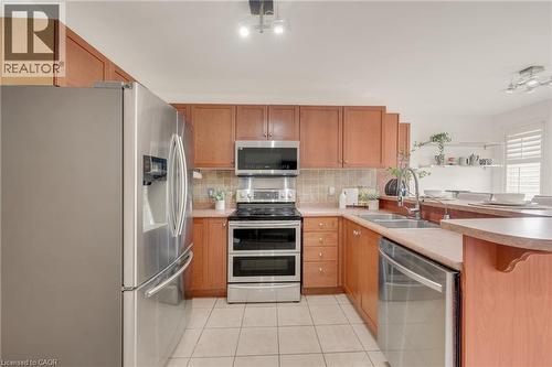 Kitchen featuring wood cabinetry, stainless steel appliances, a double basin sink, light-toned countertops, and tile flooring - 409 Jacqueline Boulevard, Hamilton, ON 