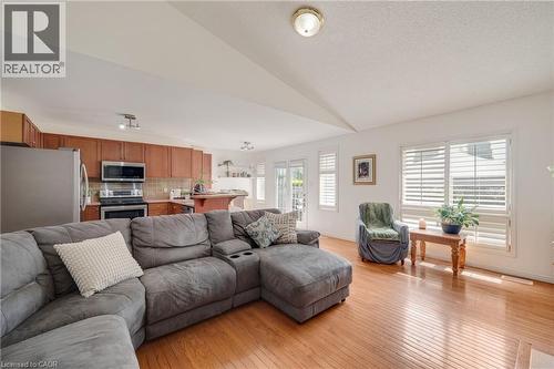 Open-concept living space featuring wood-finish flooring, white walls, and a kitchen with warm wood cabinetry and stainless steel appliances - 409 Jacqueline Boulevard, Hamilton, ON 