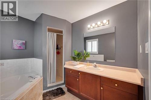 Bathroom featuring a built-in tub with tiled surround, a separate shower stall with tiled walls, a wood-finish vanity with an integrated sink, a light-toned countertop, and a large wall-mounted mirror - 409 Jacqueline Boulevard, Hamilton, ON 