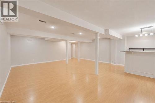 Expansive finished lower level featuring light wood-finish flooring, recessed lighting, and a built-in wet bar with white cabinetry and a light-toned countertop. Furniture has been removed. - 409 Jacqueline Boulevard, Hamilton, ON 