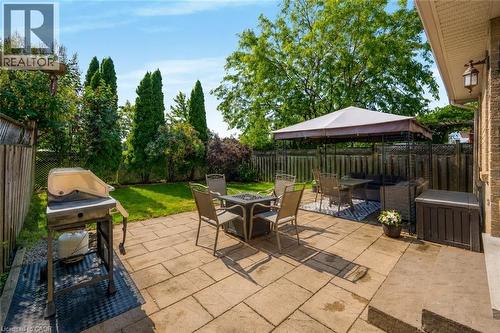 Expansive backyard featuring a stone patio, manicured lawn, and mature perimeter trees - 409 Jacqueline Boulevard, Hamilton, ON 