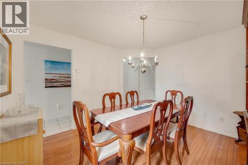 Bright dining area featuring wood-finish flooring, a contemporary chandelier, and direct access to another room with tiled flooring - 409 Jacqueline Boulevard, Hamilton, ON 