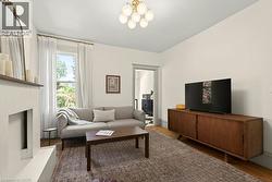 Living room featuring wood-finish flooring, a contemporary fireplace, and a large window with exterior foliage visible - 