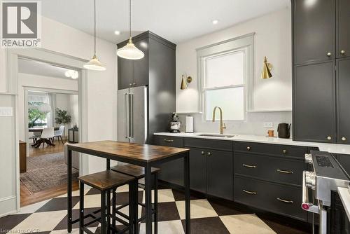 Kitchen featuring dark cabinetry with gold-toned hardware, stainless steel refrigerator, white countertops, and checkerboard flooring - 148 Dundurn Street N, Hamilton, ON 