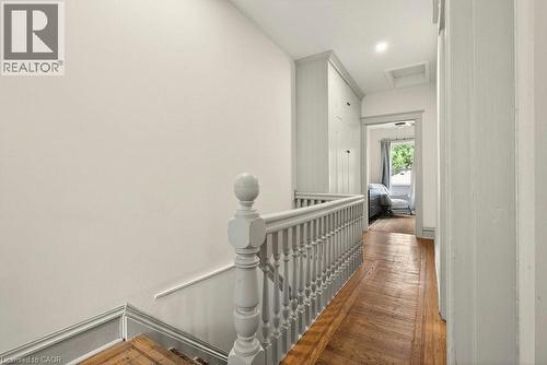 Hardwood flooring throughout the upper hallway with a light-toned staircase railing and built-in vertical cabinetry - 148 Dundurn Street N, Hamilton, ON 