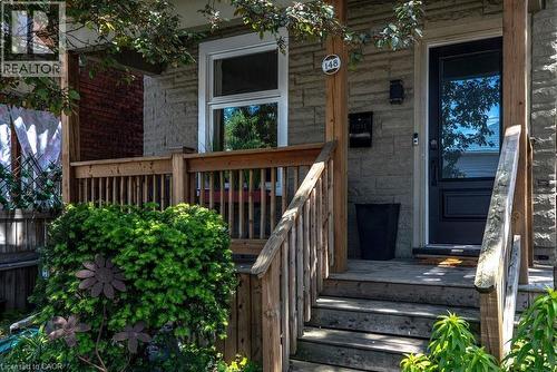 Inviting front porch featuring natural wood railings and steps, stone-finish siding, a dark paneled entry door with an integrated window, and a wall-mounted mailbox - 148 Dundurn Street N, Hamilton, ON 