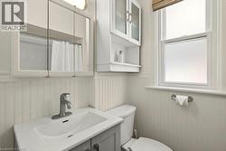 Bathroom featuring a single-sink vanity with a chrome faucet, beadboard wainscoting, an overhead mirrored medicine cabinet, and a window with a privacy film - 