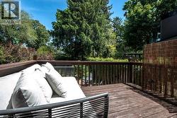 Spacious outdoor deck featuring wood-finish decking, a sturdy wooden railing, and mature green foliage surrounding the property - 