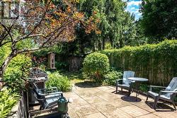Expansive backyard with a paver patio area, mature trees, lush greenery, and a wood privacy fence - 