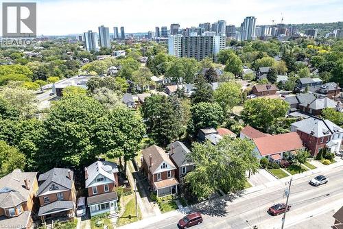 Aerial view of a residential street with detached homes featuring various architectural styles, mature trees, and a distant cityscape - 148 Dundurn Street N, Hamilton, ON 