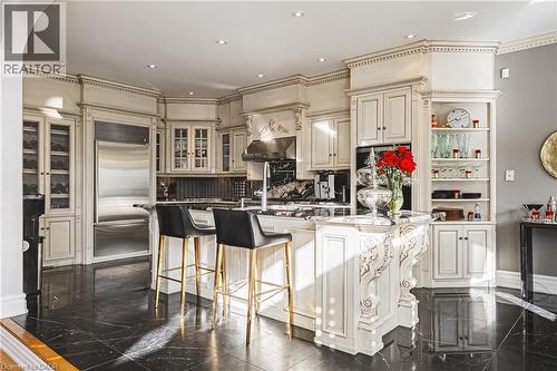 Gourmet kitchen featuring custom cabinetry, integrated stainless steel refrigerator, black stone flooring, and a central island with carved corbels - 712 Highvalley Road, Ancaster, ON 