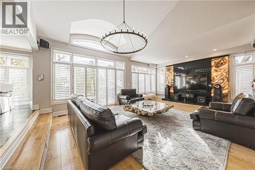 Spacious living area featuring extensive windows with white plantation shutters, a vaulted ceiling, and a large circular chandelier - 712 Highvalley Road, Ancaster, ON 