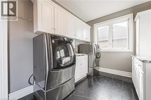 Laundry area featuring white cabinetry, a large window, dark tile flooring, and light gray walls - 712 Highvalley Road, Ancaster, ON 