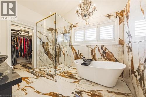 Spacious bathroom featuring large format marble-look tile flooring and walls, a freestanding soaking tub, and a frameless glass shower enclosure with brass-finish hardware - 712 Highvalley Road, Ancaster, ON 
