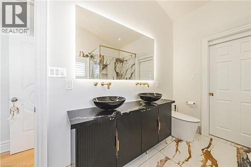 Double vanity featuring vessel sinks, wall-mounted brass fixtures, and a back-lit mirror - 712 Highvalley Road, Ancaster, ON 