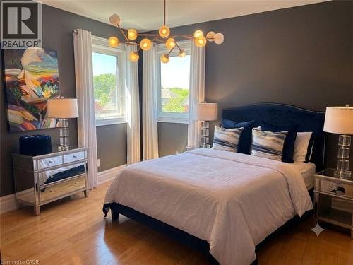 Hardwood flooring throughout this bedroom, featuring a contemporary chandelier and two large windows with white trim - 712 Highvalley Road, Ancaster, ON 