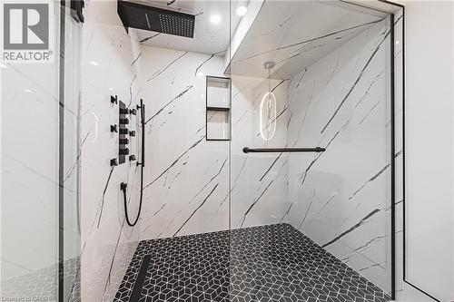Enclosed shower with full-height glass panels, black geometric floor tiling, and white marble-look wall tiling with dark veining - 712 Highvalley Road, Ancaster, ON 