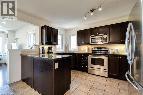 Kitchen featuring dark wood cabinetry, stainless steel appliances, a center island with a dark countertop, and light-toned floor tiles - 928 Dunblane Court, Kitchener, ON - Indoor Photo Showing Kitchen