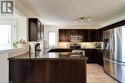 Kitchen featuring dark wood-finish cabinetry, stainless steel appliances, granite-style countertops, and tile flooring - 