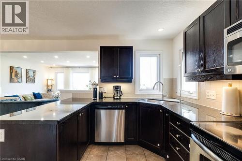 Kitchen featuring dark wood cabinetry, light-toned backsplash, stainless steel appliances, and a U-shaped countertop - 928 Dunblane Court, Kitchener, ON - Indoor Photo Showing Kitchen With Upgraded Kitchen