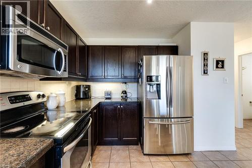 Kitchen featuring dark wood cabinetry, stainless steel appliances, a tile backsplash, composite countertops, and tile flooring - 928 Dunblane Court, Kitchener, ON - Indoor Photo Showing Kitchen