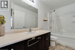 Bathroom featuring a vanity with a dark wood-finish cabinet and light-toned countertop, an undermount sink with a chrome faucet, a large wall-mounted mirror, and a white bathtub with an integrated sho - 