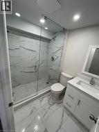 Modern bathroom featuring a frameless glass shower enclosure, white marble-look tile flooring, and a coordinating vanity with an integrated sink - 