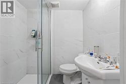 Bathroom featuring a glass-enclosed shower, white ceramic wall tiles with subtle veining, grey wood-finish flooring, a pedestal sink with chrome fixtures, and an exhaust fan - 