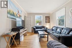Luminous living area featuring wood-finish flooring, multiple windows with blinds, and light-toned wall finishes - 
