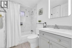 Modern bathroom featuring a white porcelain tub, patterned wall tile, a gray vanity with a single basin, a rectangular illuminated mirror, and wood-finish flooring - 
