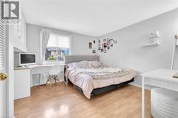 Bedroom featuring wood-finish flooring, a window with blinds and curtains, a built-in desk with overhead cabinetry, and white painted walls - 