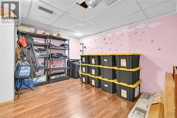 Spacious room featuring wood-finish flooring, a drop ceiling with recessed lighting, and light pink walls - 