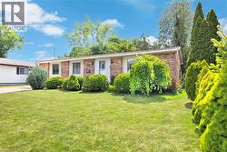 Brick exterior with a prominent front lawn, mature landscaping, and a white entry door - 