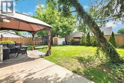 Expansive backyard featuring a concrete patio with a gazebo, a manicured lawn, a wooden privacy fence, a storage shed, and mature trees - 