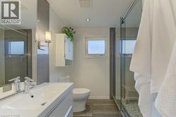 Modern bathroom featuring a single vanity with integrated sink, glass-enclosed shower with mosaic tile floor, and wood-finish flooring - 