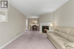 Living area featuring a fireplace with a white mantel and black surround, crown molding, and light-toned carpeting - 