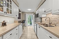 Galley kitchen featuring white cabinetry with dark ornate hardware, under-cabinet lighting, and a neutral tile backsplash - 