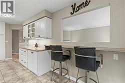Kitchen featuring white shaker cabinetry, light-toned countertops, tiled flooring, an eat-at bar, and a pass-through window - 