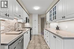 Galley kitchen featuring white cabinetry, light-toned countertops, tile flooring, and a mosaic tile backsplash - 