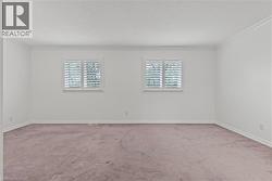 Spacious room featuring two windows with white plantation shutters, white walls, white crown molding, white baseboards, and textured carpeting - 