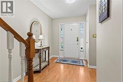 Entryway featuring wood-finish flooring, a white paneled door with sidelights, and a wood staircase with white balusters - 